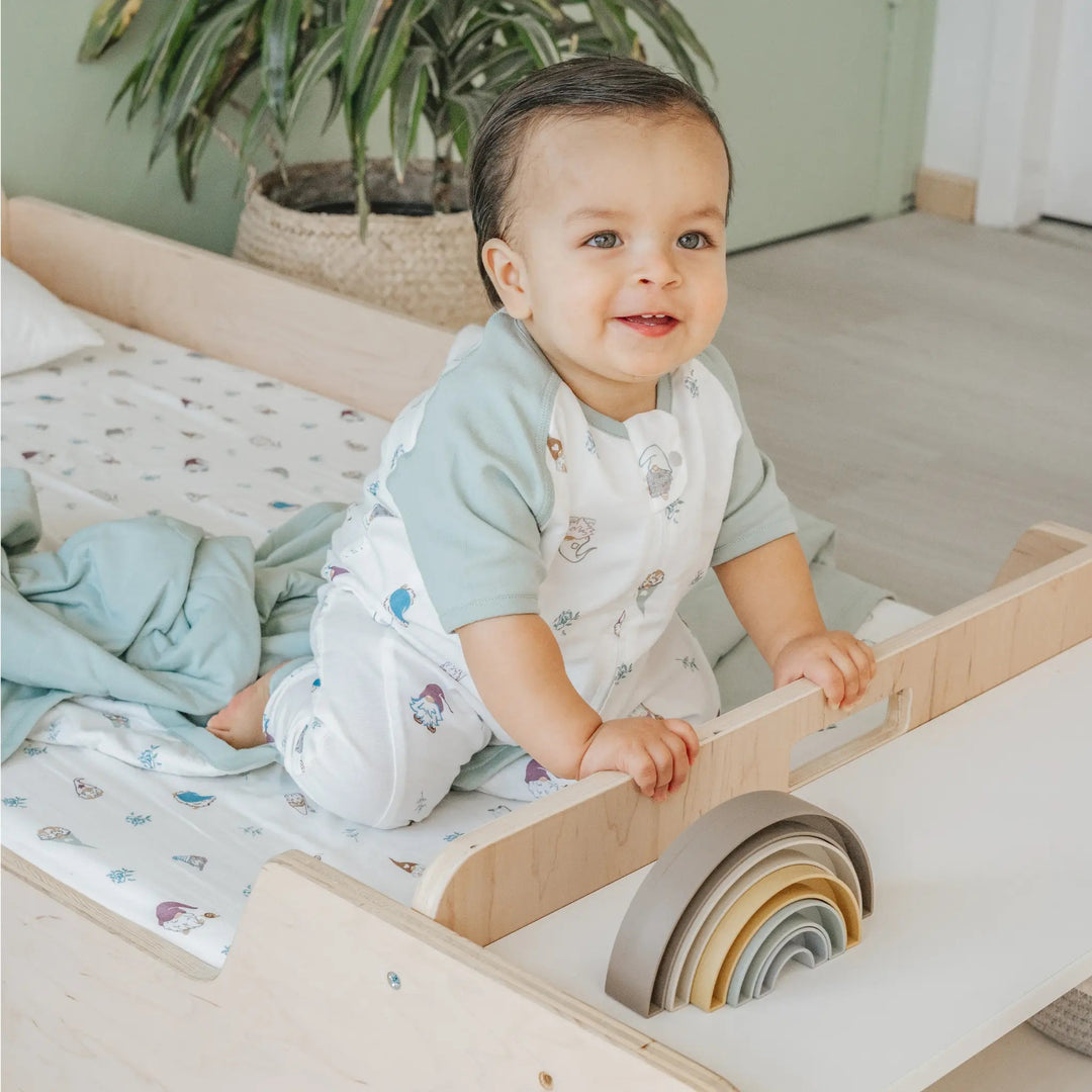 Baby playing with a wooden toy on a floor bed in a home setting