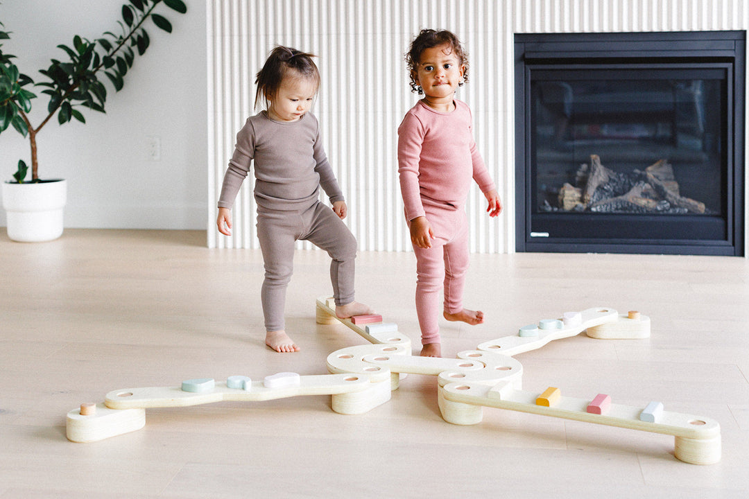 Two children playing with a wooden toy on a light wood floor.